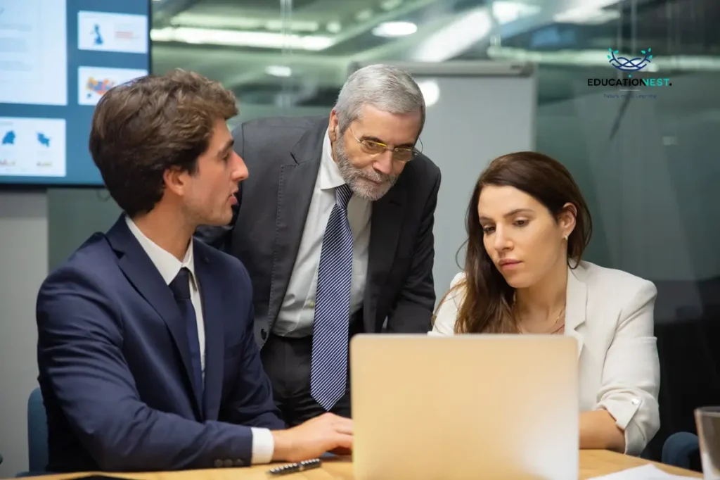 Three business professionals in a meeting room collaboratively reviewing information on a laptop regarding corporate compliance.