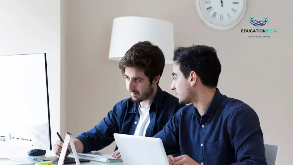 Two men at a desk with a laptop, discussing Microsoft Copilot vs. ChatGPT features and functionalities.