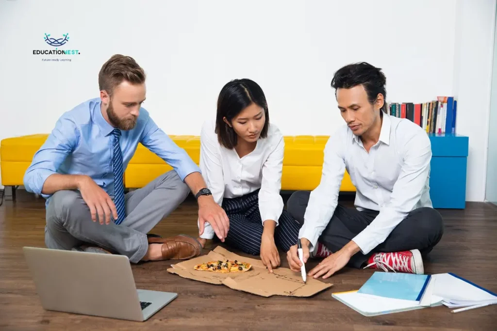 Three business professionals seated on the floor, collaborating with a laptop during an outbound corporate training session.