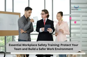 Three professionals in business attire collaborate around a table with a laptop, discussing workplace safety training.