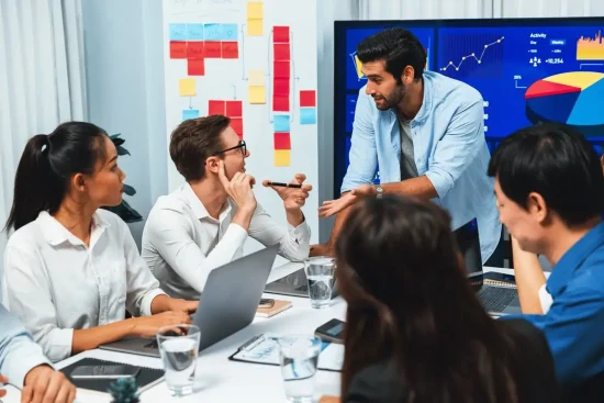 A man stands in front of a group of employees in a meeting room during a soft skills training session.