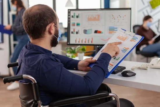 A man in a wheelchair sits at a desk, focused on a clipboard, representing his role as a Rational Performance Tester.