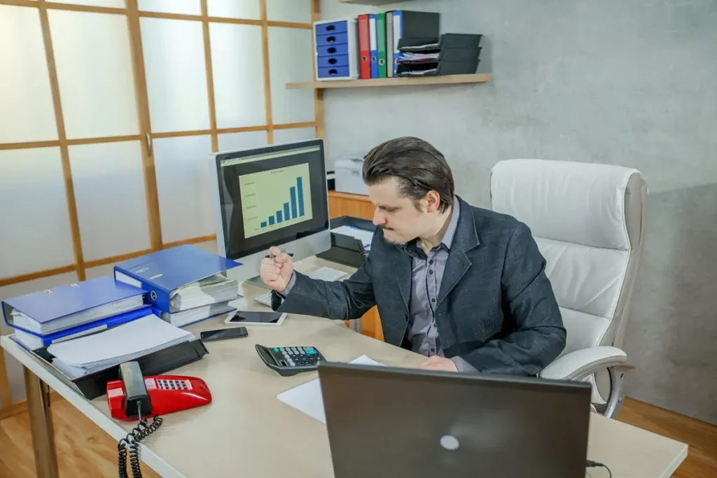 A man at a desk with a computer and phone, reflecting daily tasks of a CFO in a professional setting.
