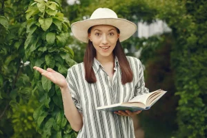 A woman in a hat holds an open book titled Environmental Literacy, engaged in reading outdoors.