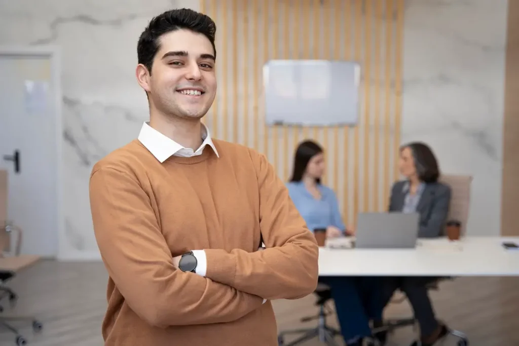 A man in an office with arms crossed, representing the theme of Apprentice vs Intern.